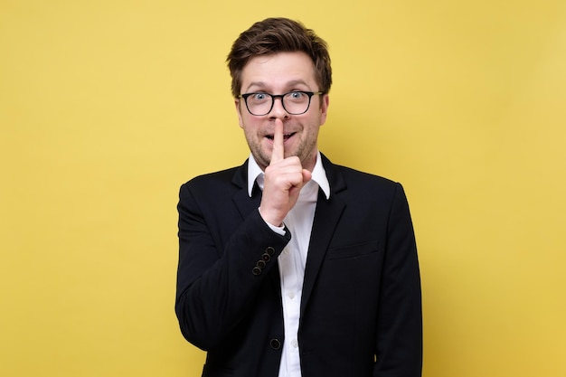 Photo man in suit over yellow background showing a sign of silence gesture