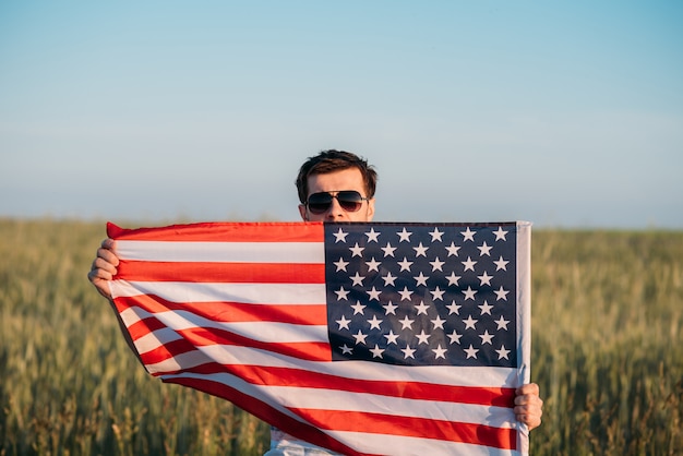 Man in sunglasses hold american flag in field. Symbol of Independence Day fourth of July in USA