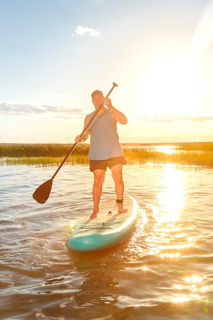 A man on a SUP board with an oar floats on the water against the background of the sunset