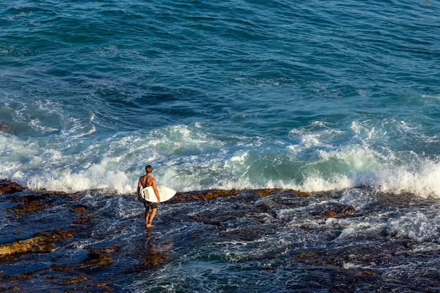 Man surfer carrying his surfboard  and waiting for the waves on ocean