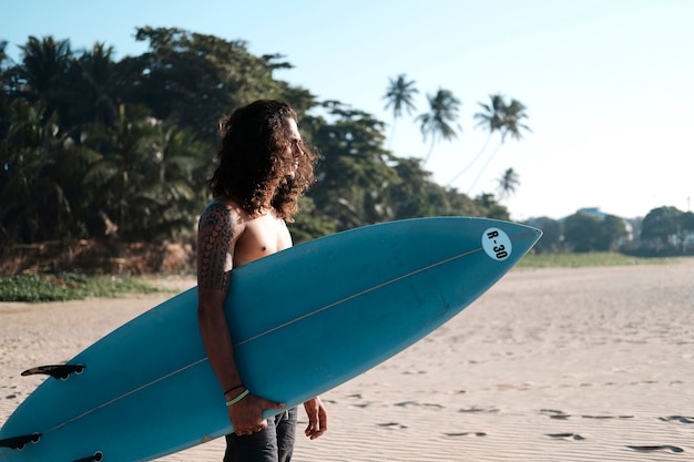 Man Surfer Sitting at Surfboard on Sand Beach