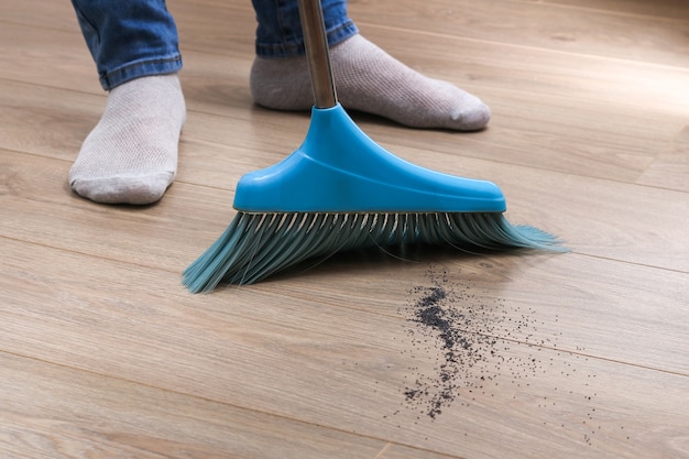 The man sweeps the debris into a blue scoop with brush.