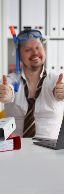 Photo man in swimming goggles shows ok gesture and holds thumbs up in office closeup