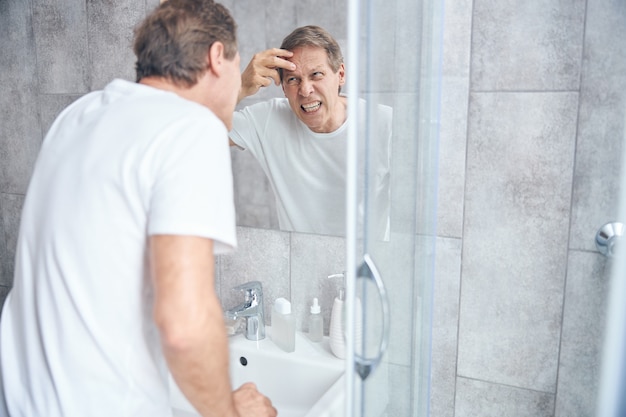 Man in a t-shirt performing a skin check in front of the mirror on the wall