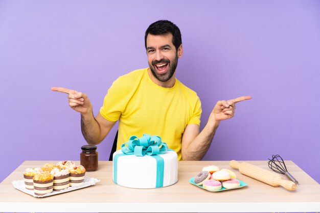 Man in a table with a big cake pointing finger to the laterals and happy