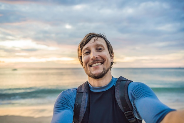 A man takes a selfie on the background of the sea and sunset