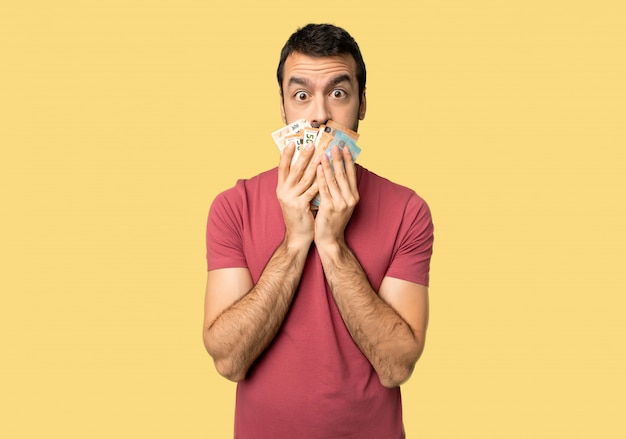 Man taking a lot of money covering mouth with hands for saying something inappropriate on isolated yellow background