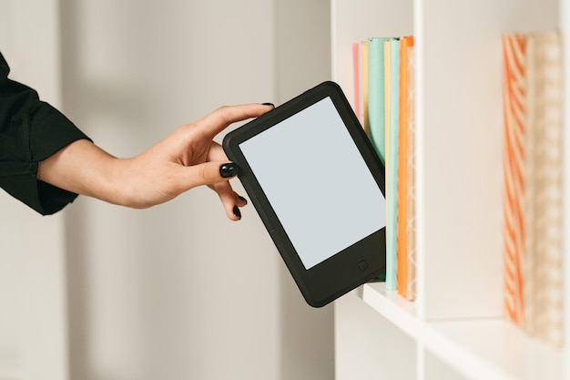 Photo man taking modern ebook reader from a bookshelf close up