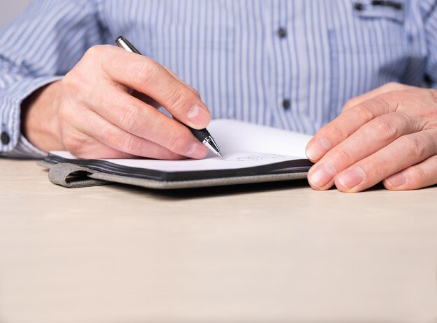 Man taking notes in planner Hands closeup writing information agenda reminders with pen in notebook Businessman sitting at desk and working or studying