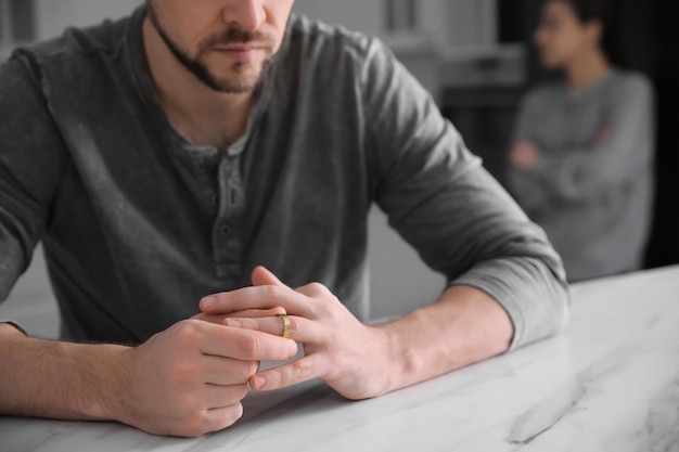 Man taking off wedding ring at white marble table indoors closeup Couple on verge of divorce