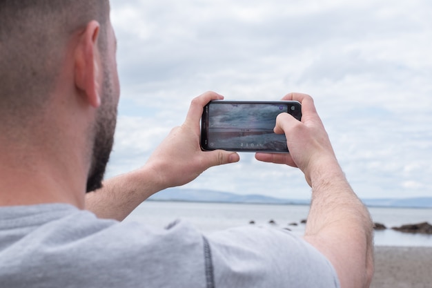 Man taking photo with mobile phone on the beach .Mountains view in the distance