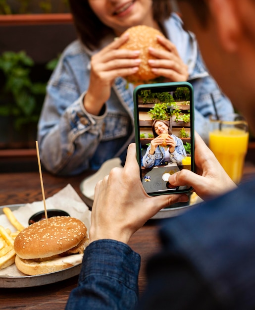 Man taking picture of woman eating burger