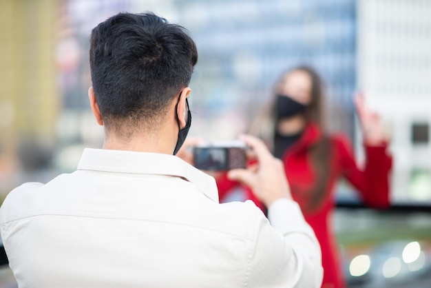 Man taking pictures of hif girlfriend outdoor wearing protective mask against covid coronavirus pandemic