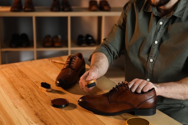 Man taking professional care of brown leather shoes in workshop closeup