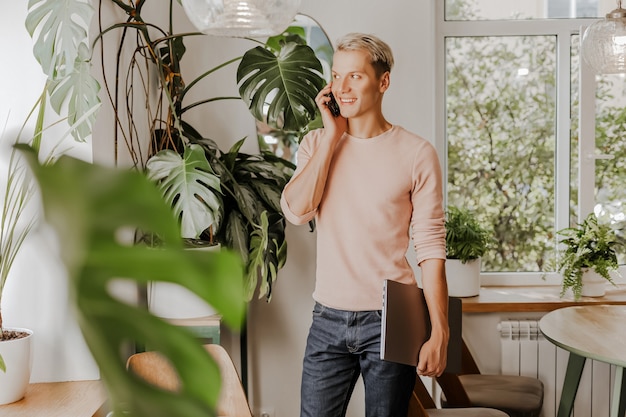 Man talking on the phone, businessman with laptop in workspace in eco cafe with plants