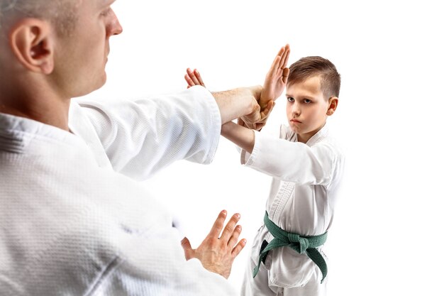 Man and teen boy fighting at Aikido training in martial arts school. Healthy lifestyle and sports concept. Fightrers in white kimono on white wall. Karate men with concentrated faces in uniform.