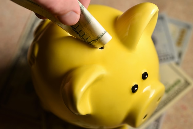 man throws a bill into a yellow piggy bank.