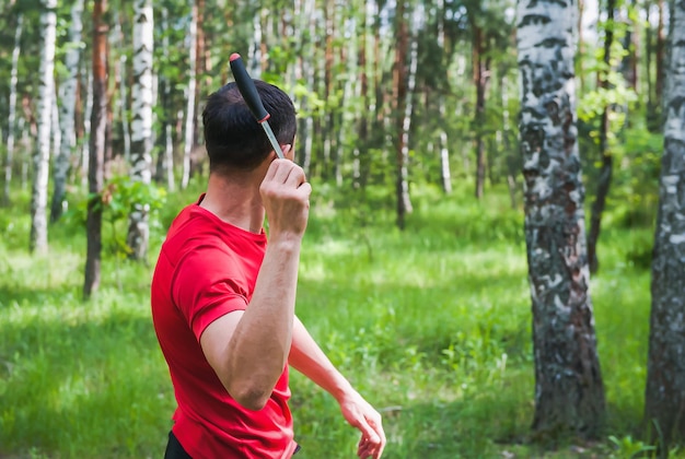 A man throws a knife at a target in the summer forest back view Throwing a knife