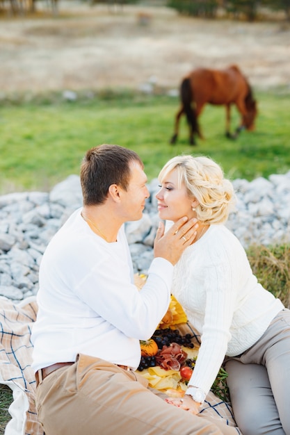 Man touches his hand to woman's cheek while sitting on a blanket brown horse grazing