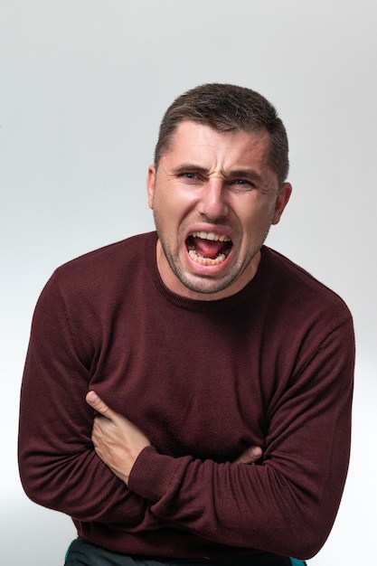 A man touches his stomach with two hands on a white background with copy space Stomach pain in a man