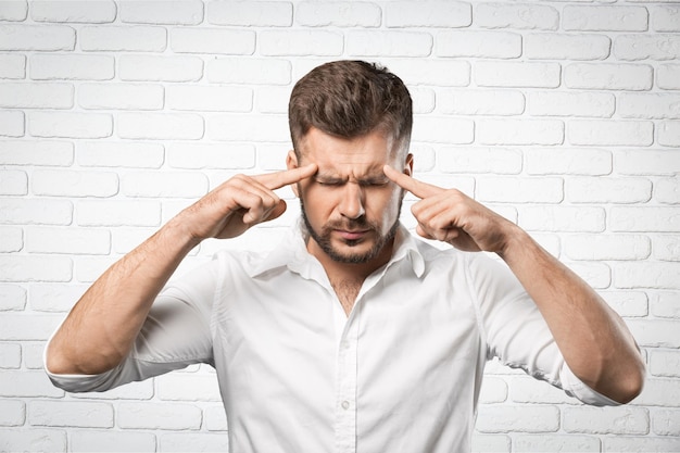 Man touching head with fingers, having headache on brick background