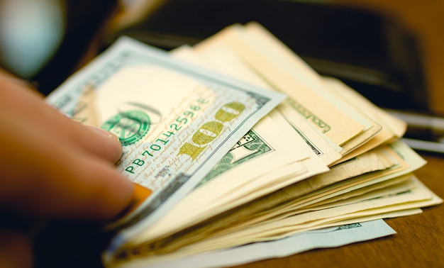 A man touching a wad of US dollar bills which is on the wooden table