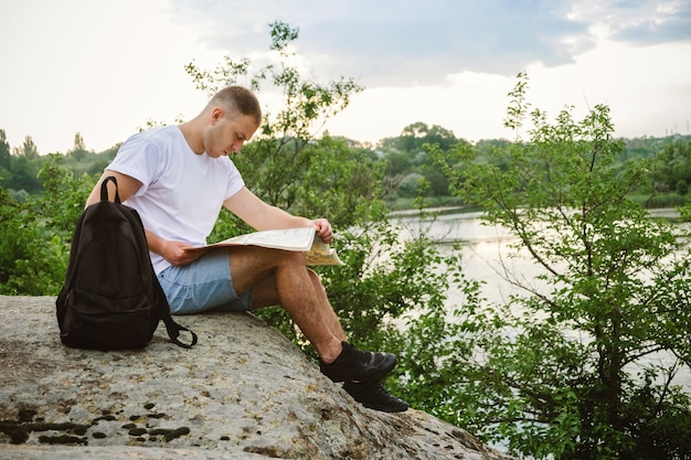 Man tourist sitting on a stone by the river read the map.