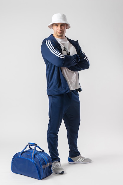 A man in a tracksuit stands near a large blue sports bag