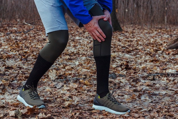 man in training clothes got a knee injury while jogging in outdoor workout. Concept of sports injury, running technique, wrong running, tendonitis, a large load.