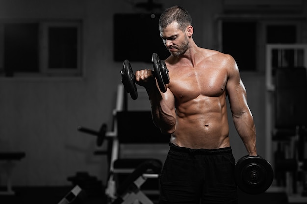 Man trains in the gym Athletic man trains with dumbbells, pumping his biceps