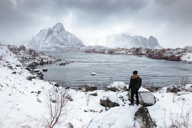 Man traveler standing on rock with Reine village view in blizzard