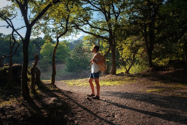 Man Traveler with backpack hiking outdoor in summer sunset forest