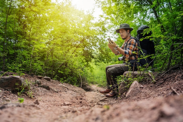 Man traveler with backpack using smartphone in the forest