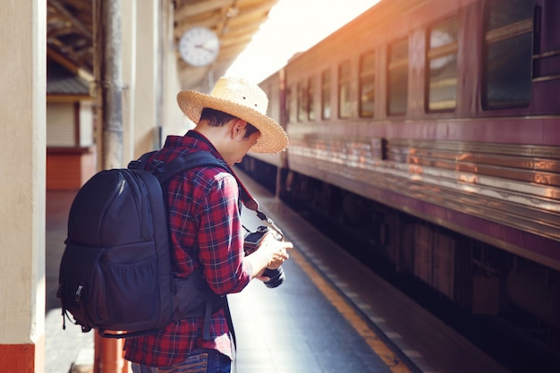 Photo man traveler with photo camera and backpack stand on railroad station