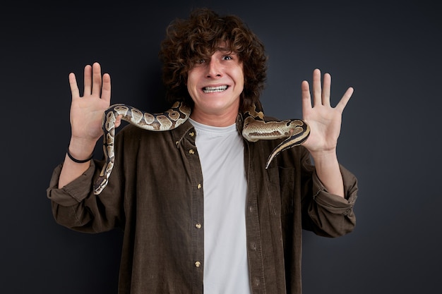 Man trying to keep calm while exotic snake is crawling on him, isolated over black background