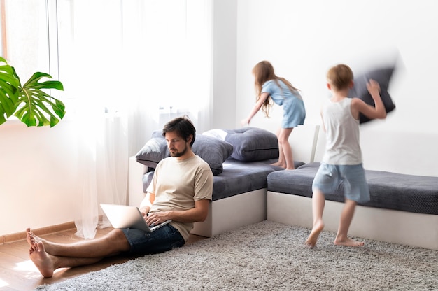 Man trying to work on laptop from home while her children are running around