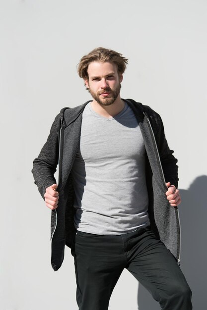 Man in tshirt and warm coat pose on sunny day on grey wall. Sport fashion, style, sportswear concept