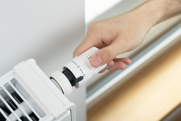 The man turns off the heating by setting the radiator thermostat to a minimum