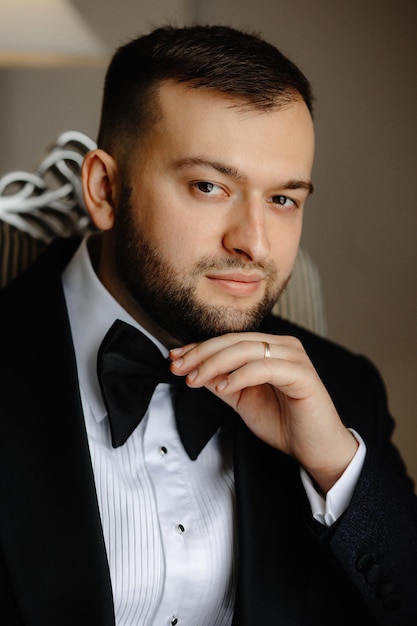 A man in a tuxedo is sitting in a chair and wearing a bow tie.