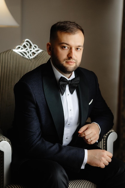 A man in a tuxedo sits in a chair.