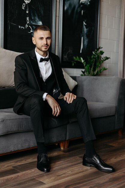 Photo a man in a tuxedo sits on a couch in front of a window