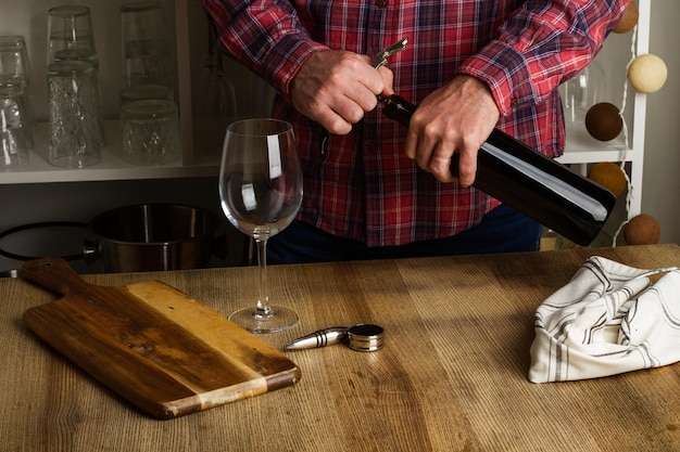 Man uncorking a bootle of red wine on a wooden table