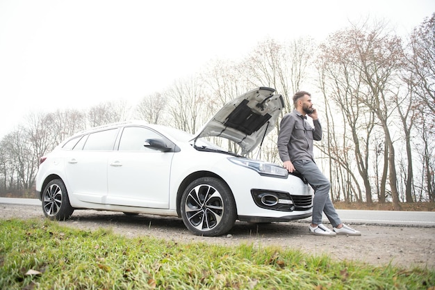 Man use a cellphone call garage in front of the open hood of a broken car on the road in the forest Car breakdown concept