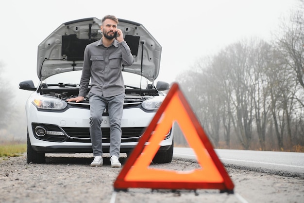 Man use a cellphone call garage in front of the open hood of a broken car on the road in the forest Car breakdown concept