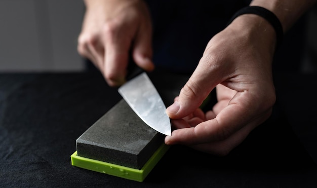 Man uses natural sharpening whetstone to sharpen big kitchen knife against black background