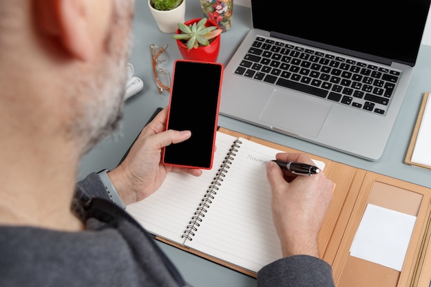 Man using cell phone and writing MONDAY in agenda near laptop close up. Business concept