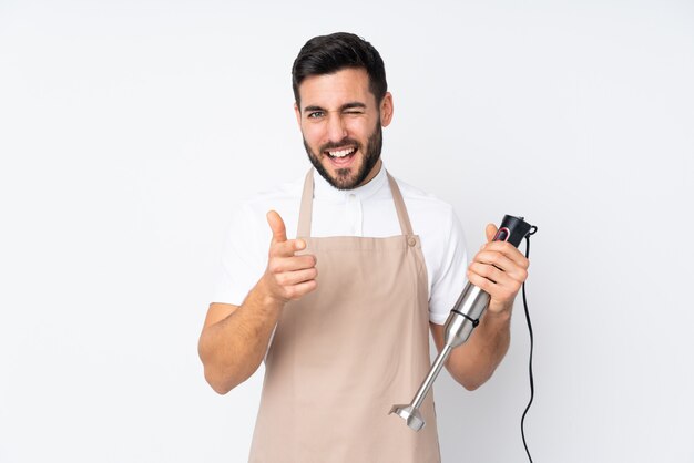 Man using hand blender on white wall points finger at you