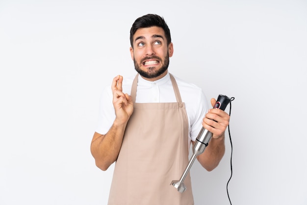 Man using hand blender on white wall with fingers crossed