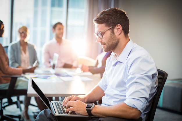 Man using laptop while coworker interacting in the background