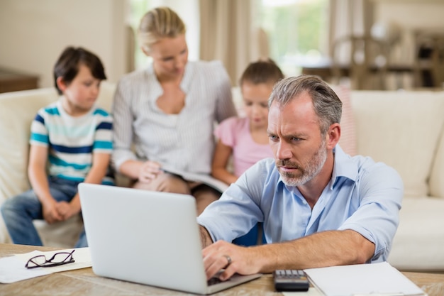 Man using laptop with bills on table in living room